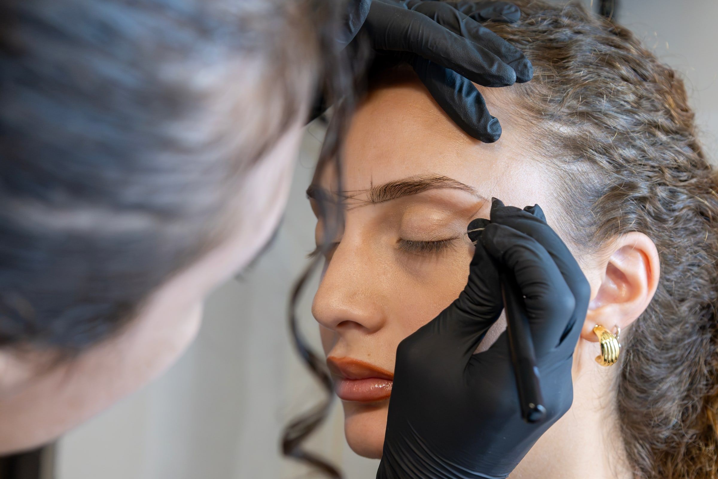 Morgana, di spalle, prepara la mappatura delle sopracciglia sul viso della cliente